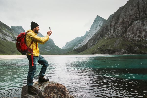 A man standing on a rock taking a picture of a lake