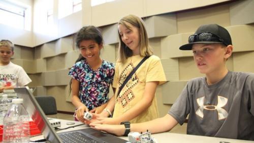 Three kids standing over computer