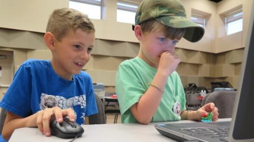 Two kids standing over a computer